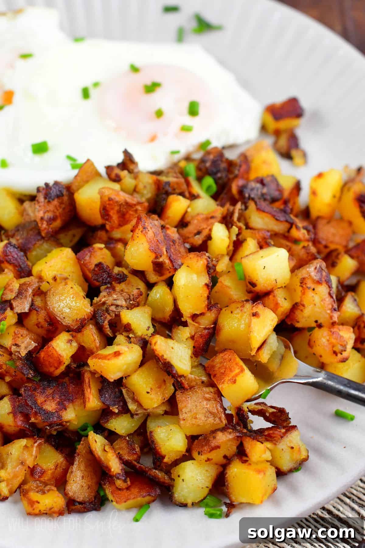 A fork scooping up a portion of freshly made, crispy home fries from a plate, highlighting their texture.