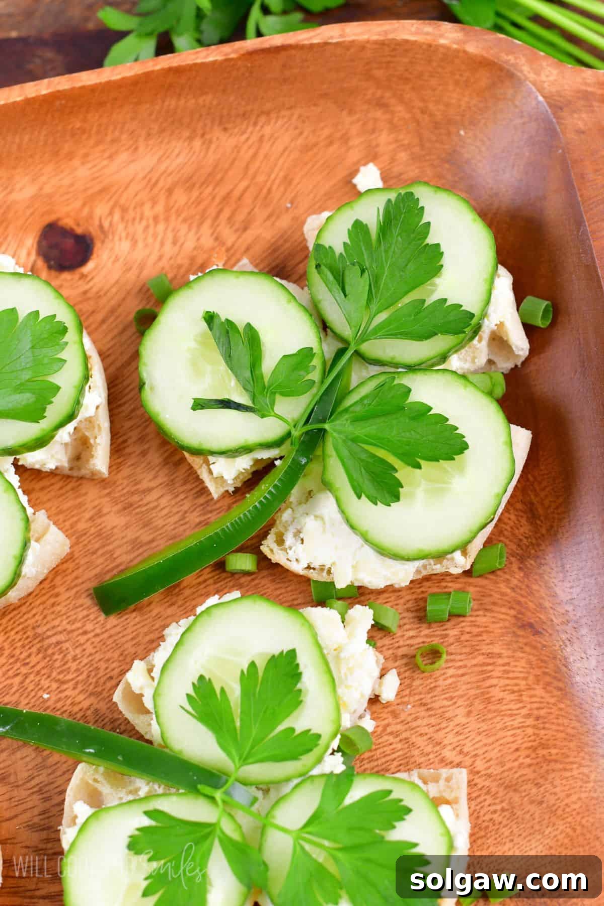 Shamrock sandwiches on a wood plater with green onions as a garnish around them.