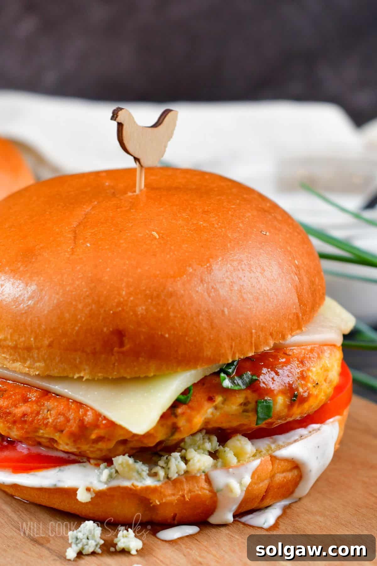 Zesty Buffalo Chicken Burger 2 A single buffalo chicken burger is presented on a wooden surface, showcasing its vibrant toppings and perfectly cooked patty.