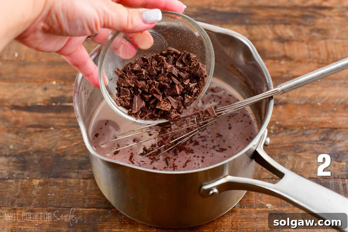 Finely chopped bittersweet chocolate being added to a saucepan of warm milk on a stovetop, ready to be whisked in.