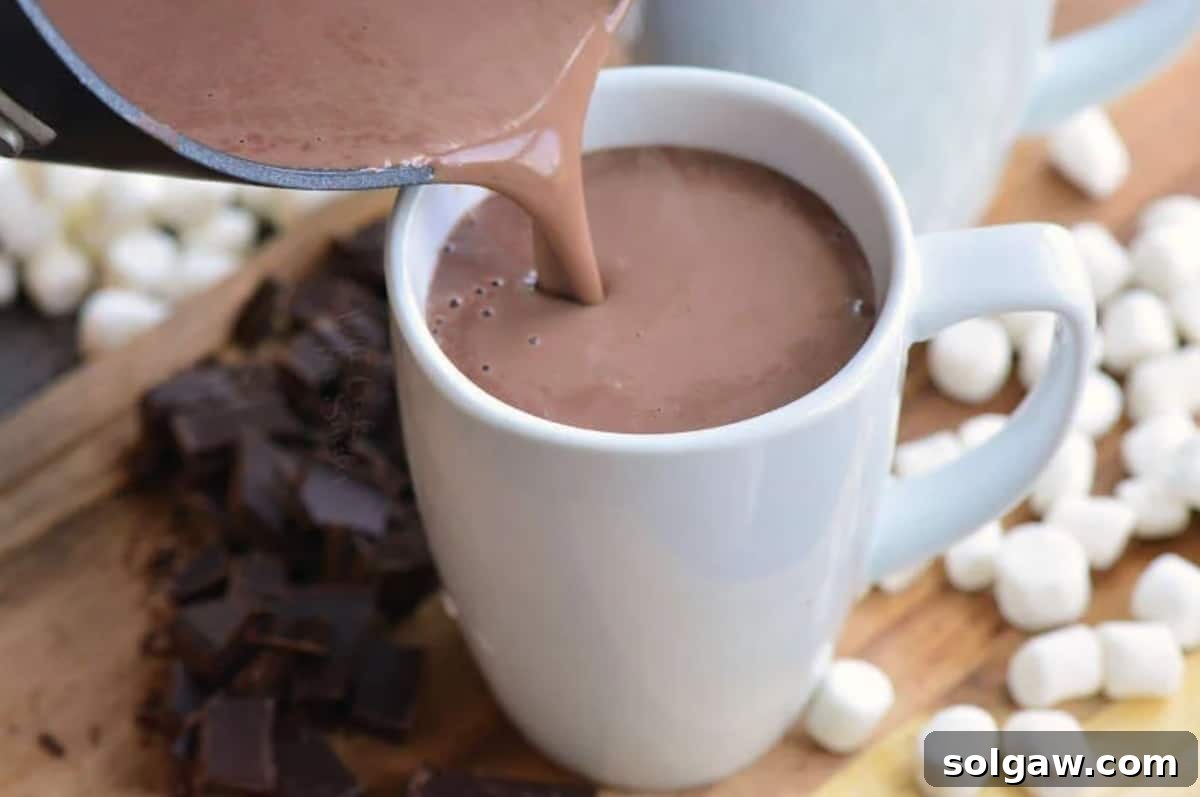 Rich, dark hot chocolate being poured from a saucepan into a white ceramic mug, creating a welcoming stream.