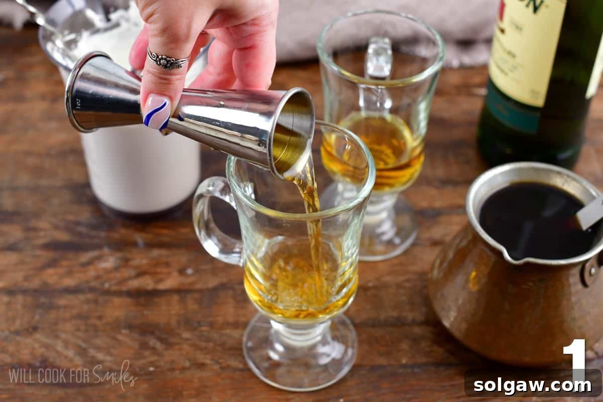 Adding Irish whiskey into a clear glass mug, with a coffee pot nearby.