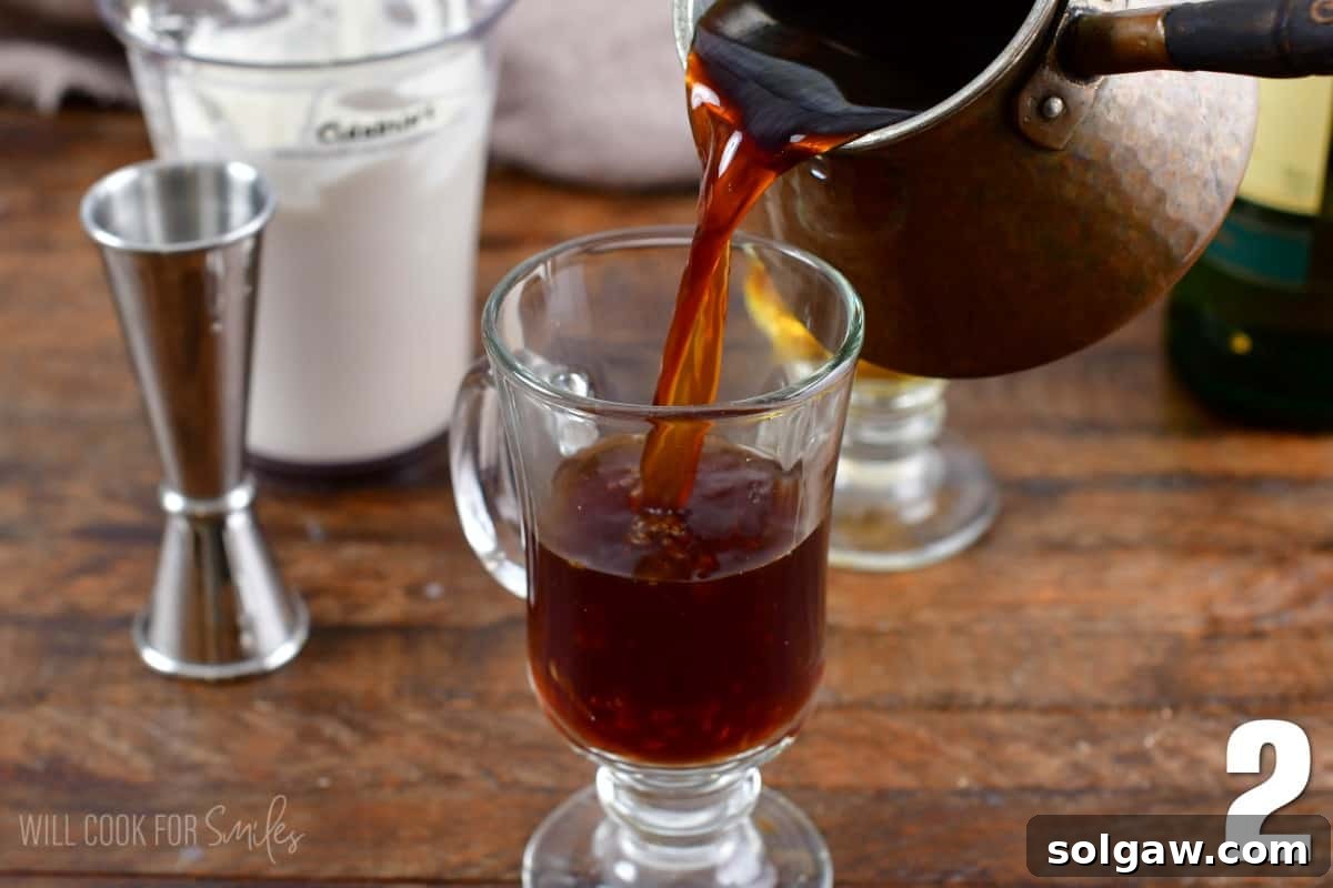 Pouring hot, strong coffee into a glass containing whiskey and sugar for an Irish coffee.