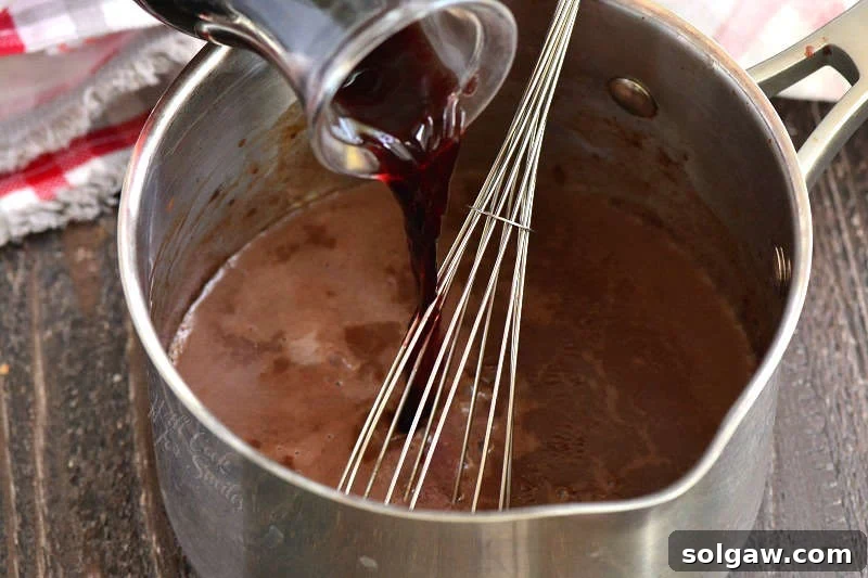 pouring wine into hot chocolate mixture that is in a pan with a wire whisk