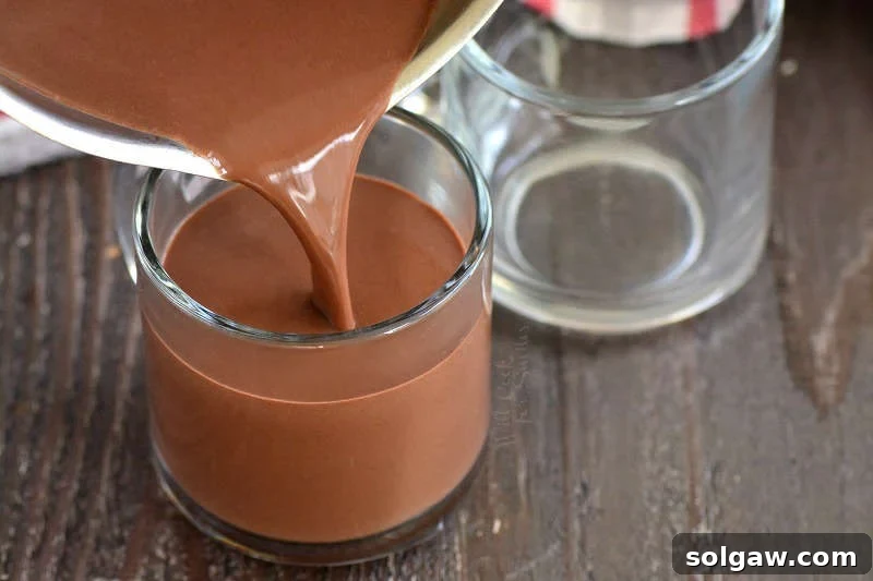 pouring hot chocolate into glasses that are on a wood cutting board