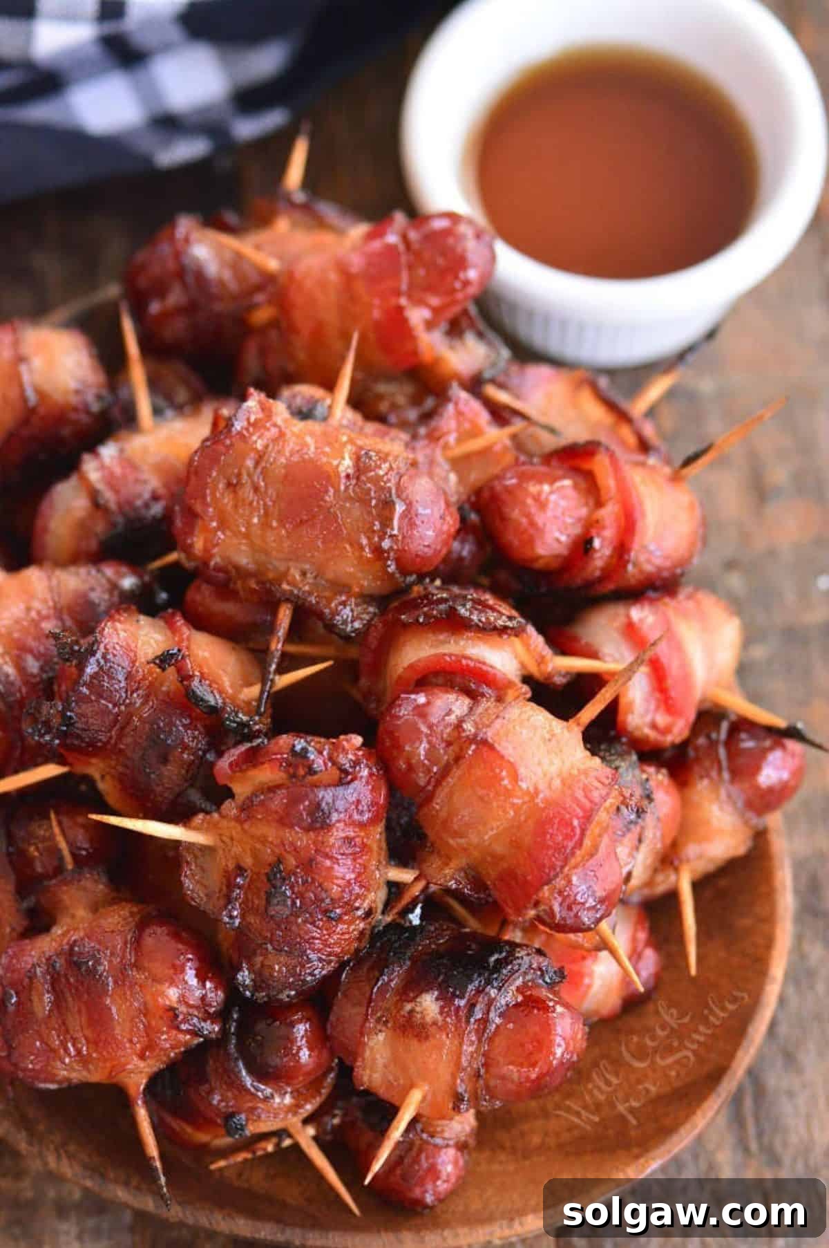 A small cluster of bacon-wrapped little smokies sausages next to a rustic bowl of maple syrup, ready to be enjoyed as a savory sweet treat.