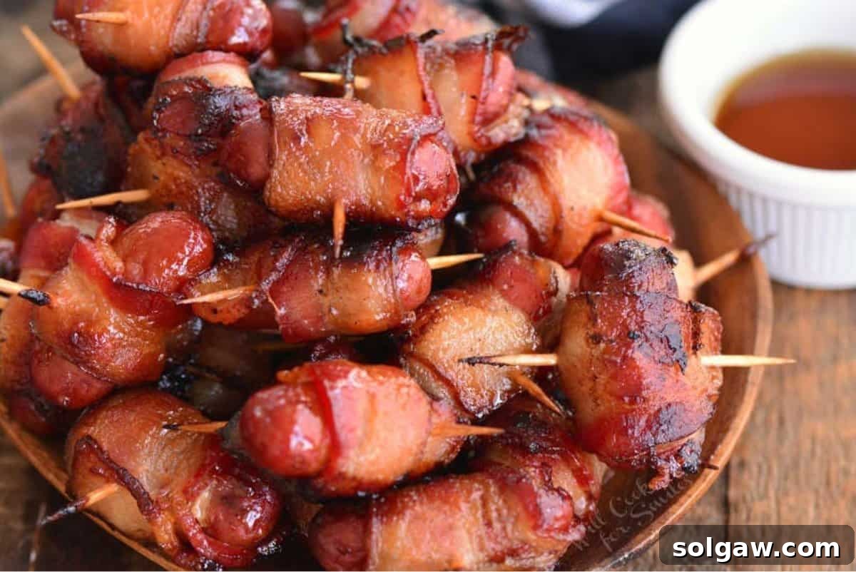 Crispy baked bacon-wrapped little sausages stacked on a plate.