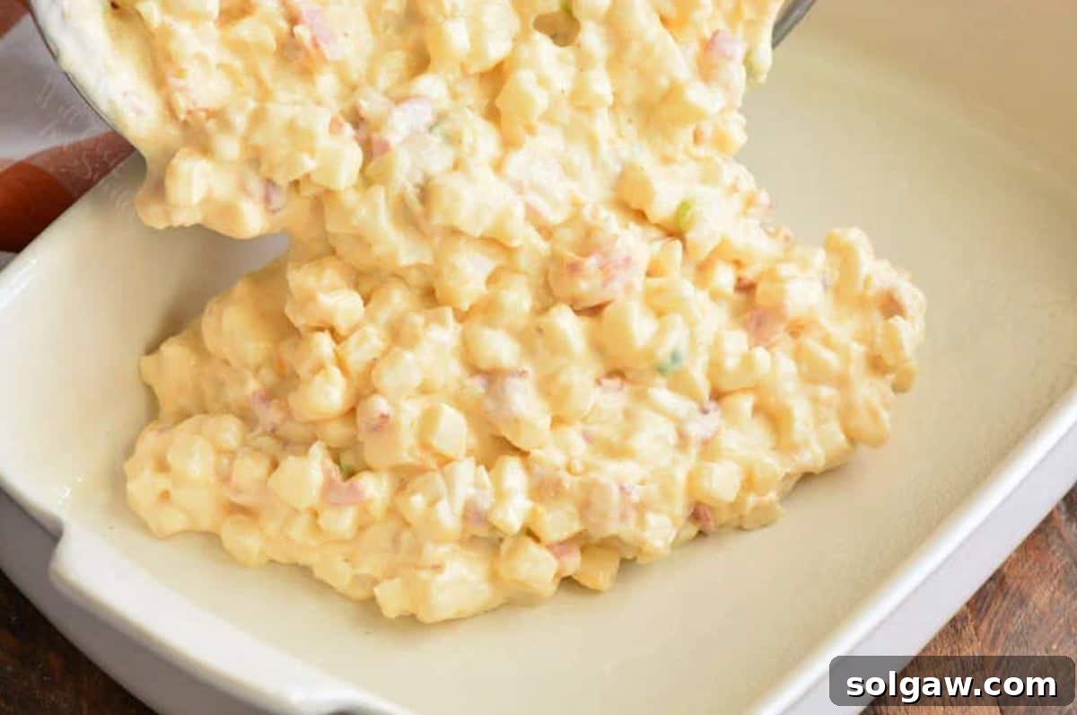 The process of preparing the loaded cheesy potato casserole. A large baking dish is being filled with the creamy, cheesy potato mixture, ready for baking.