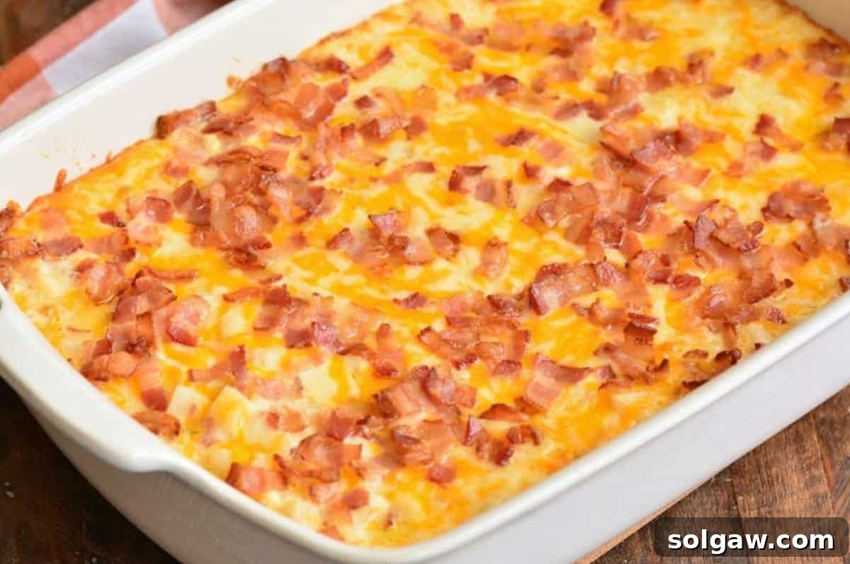 A freshly baked loaded cheesy potato casserole, golden and bubbly, with perfectly melted cheese and crispy bacon, presented in a ceramic baking dish on a rustic wooden surface.