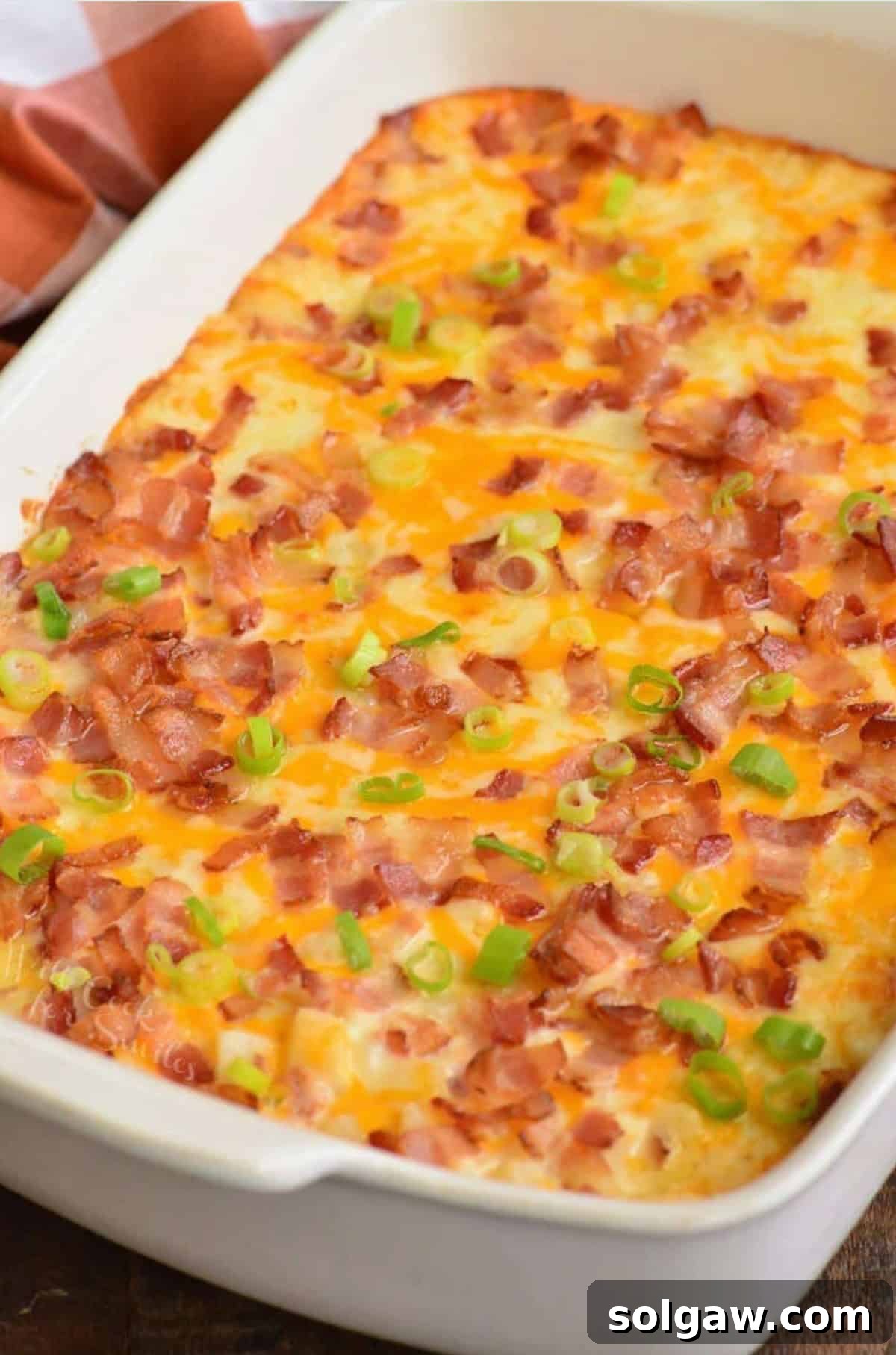 A beautifully baked loaded cheesy potato casserole, generously topped with crispy bacon and vibrant green onions, ready to be served and enjoyed.