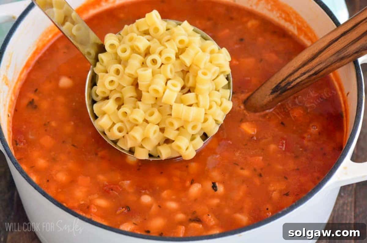 adding ladlefuls of ditalini pasta to the pasta e fagioli soup.
