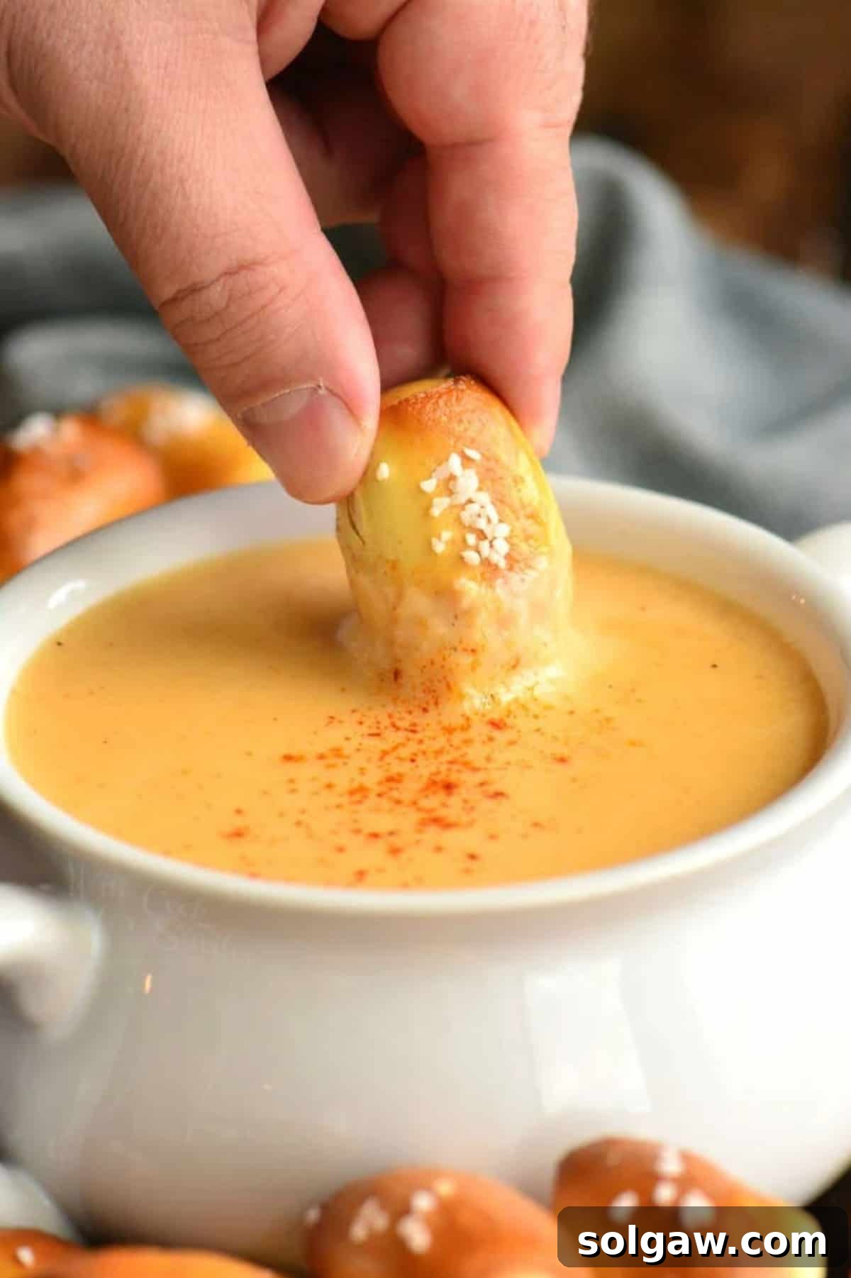 dipping a pretzel bite into the beer cheese dip in a bowl.