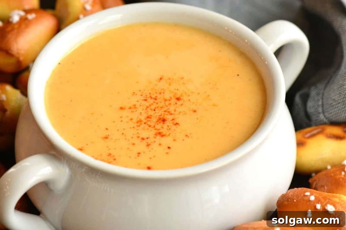 beer cheese dip topped with some paprika and pretzel bites around.