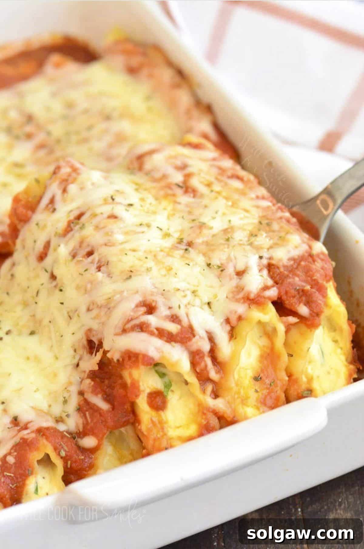 Irresistible Baked Manicotti 2 Pulling out a perfectly baked manicotti from a white baking dish with a silver spatula, showcasing melted cheese and rich sauce, ready to be served.