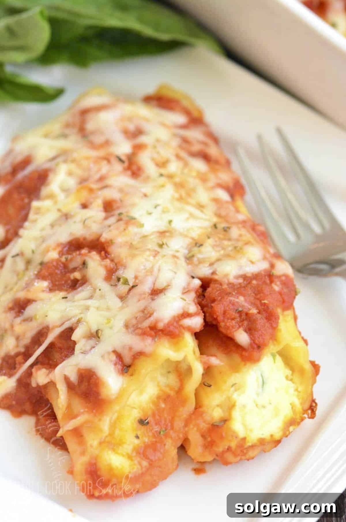 Irresistible Baked Manicotti 7 Two perfectly stuffed manicotti shells, rich with sauce and melted cheese, presented on a pristine white plate, garnished with fresh basil leaves.