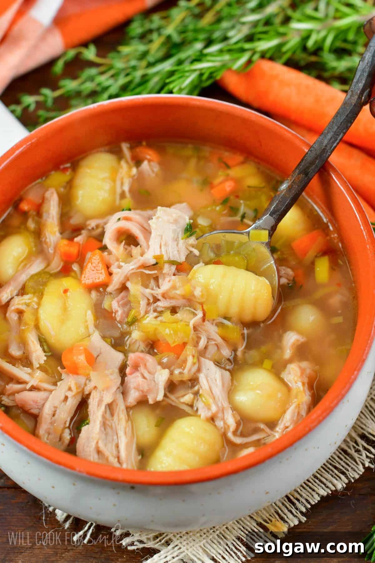 spooning out some chicken gnocchi soup from the bowl with a spoon.