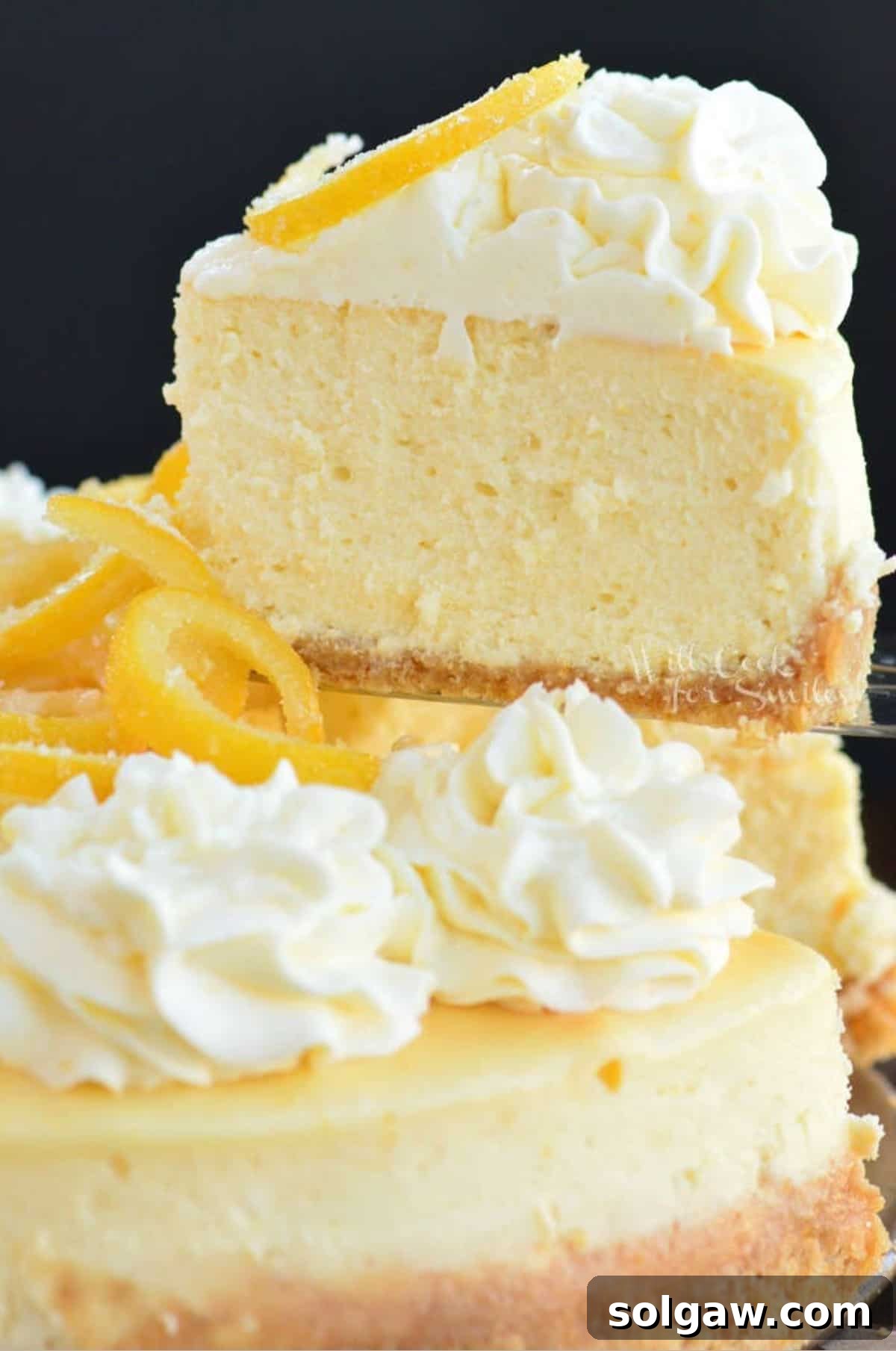 A hand pulling out a perfect slice of lemon cheesecake, revealing its creamy texture and crust.