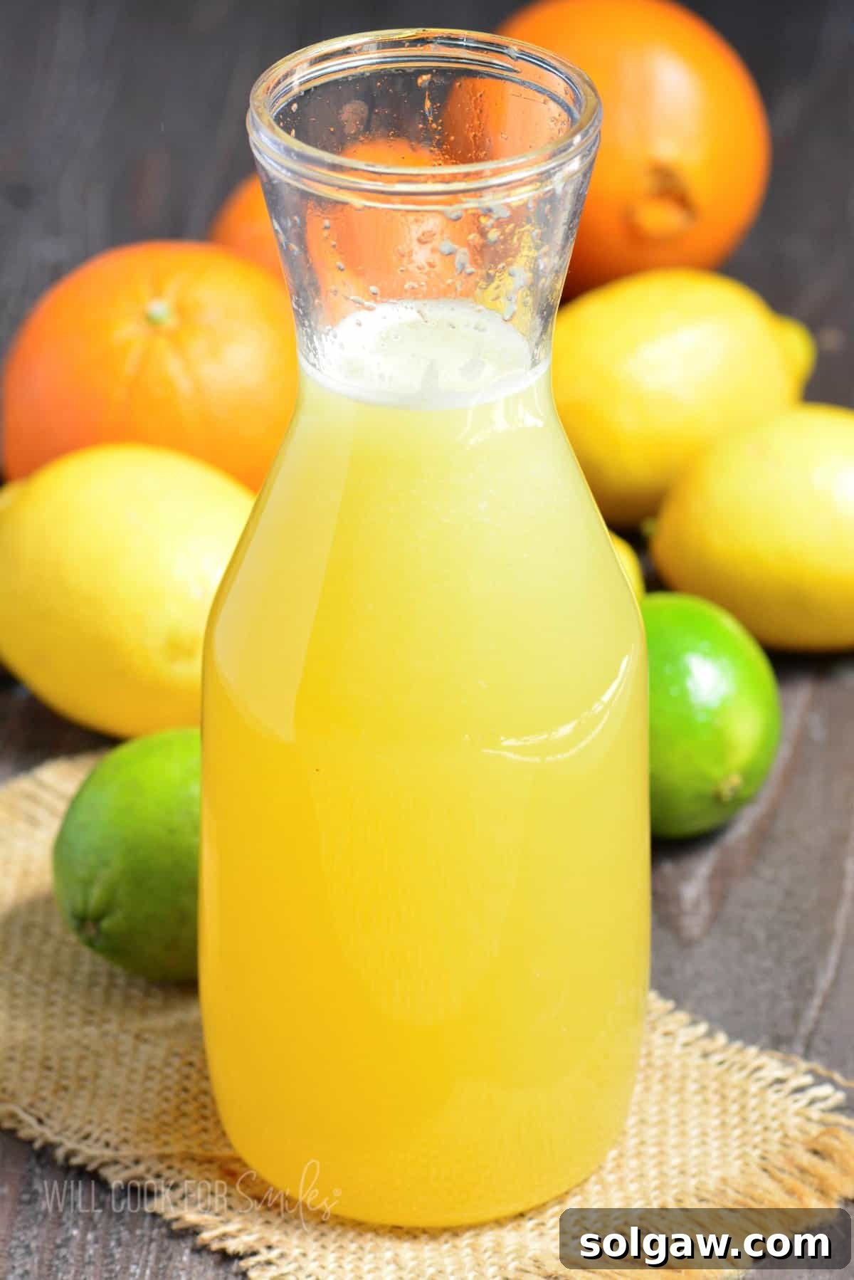 Tall bottle filled with a bright, vibrant homemade margarita mix, surrounded by fresh citrus fruits like limes, lemons, and oranges, ready for crafting delicious cocktails.