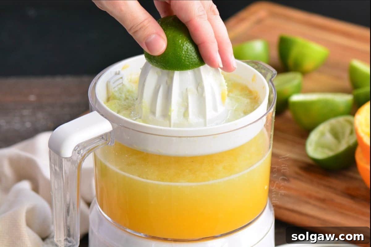 Close-up shot of a hand holding a lime half over an electric citrus juicer, demonstrating the process of extracting fresh juice for the margarita mix.