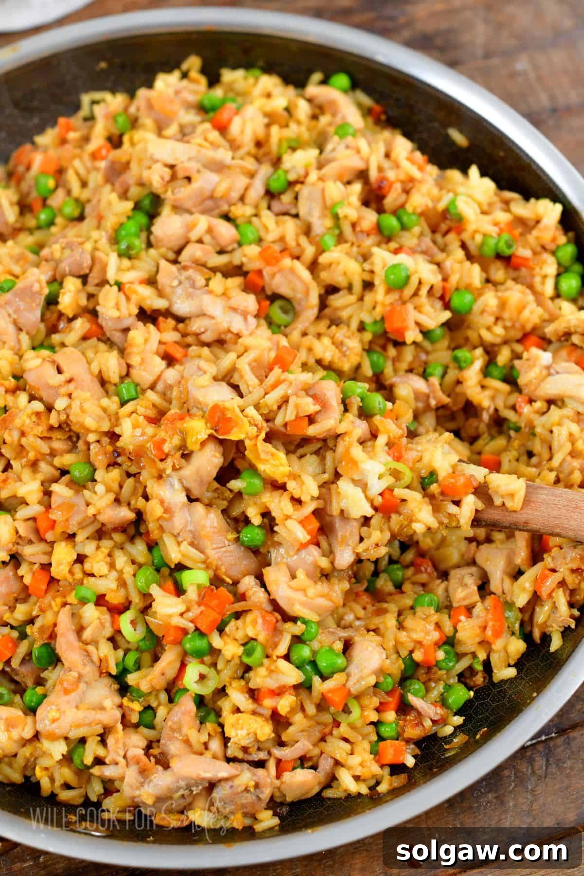chicken fried rice in a cooking pan with some scooped on a wooden spoon.