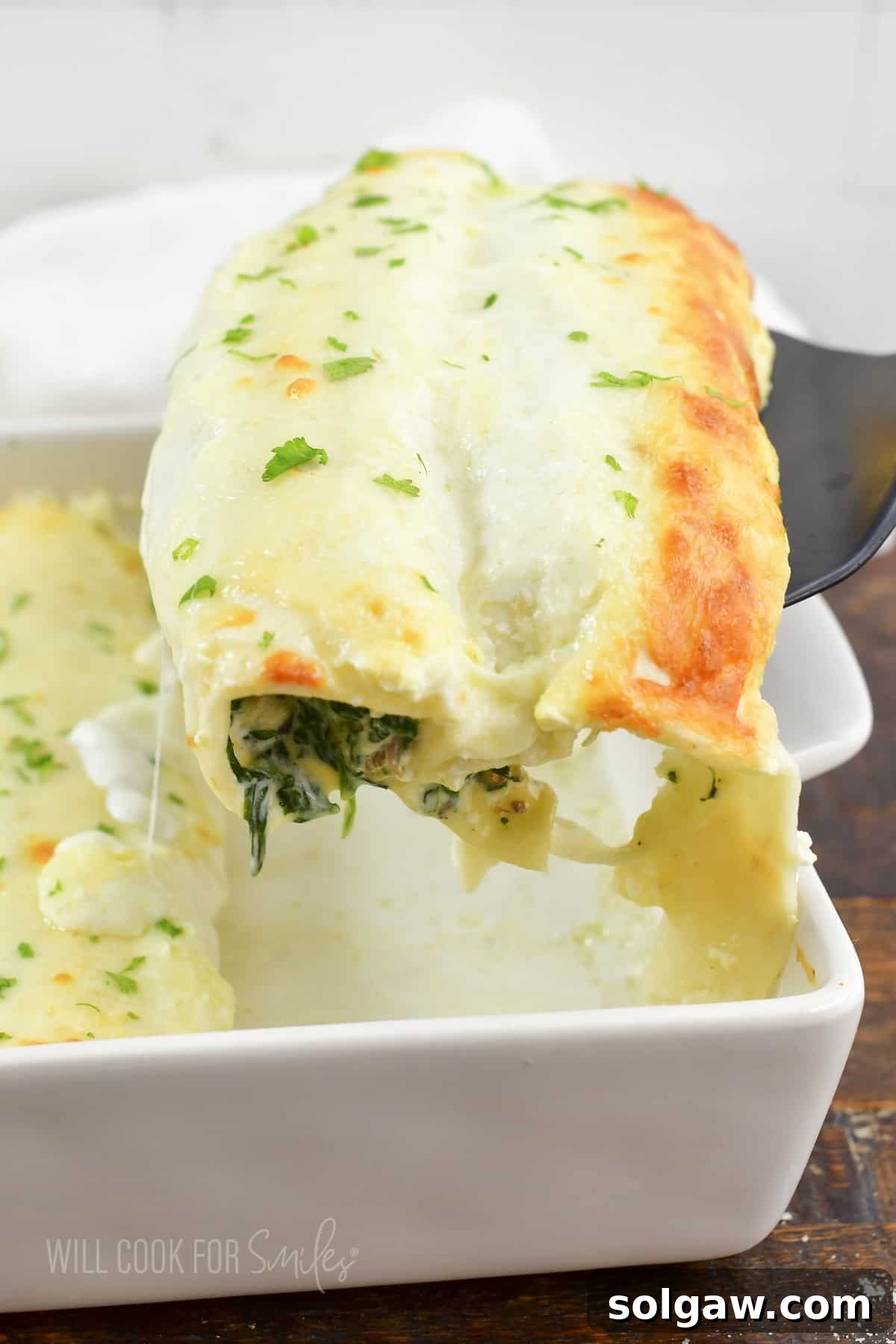 pulling out two enchiladas out of the baking dish, showing the golden cheese and creamy sauce.