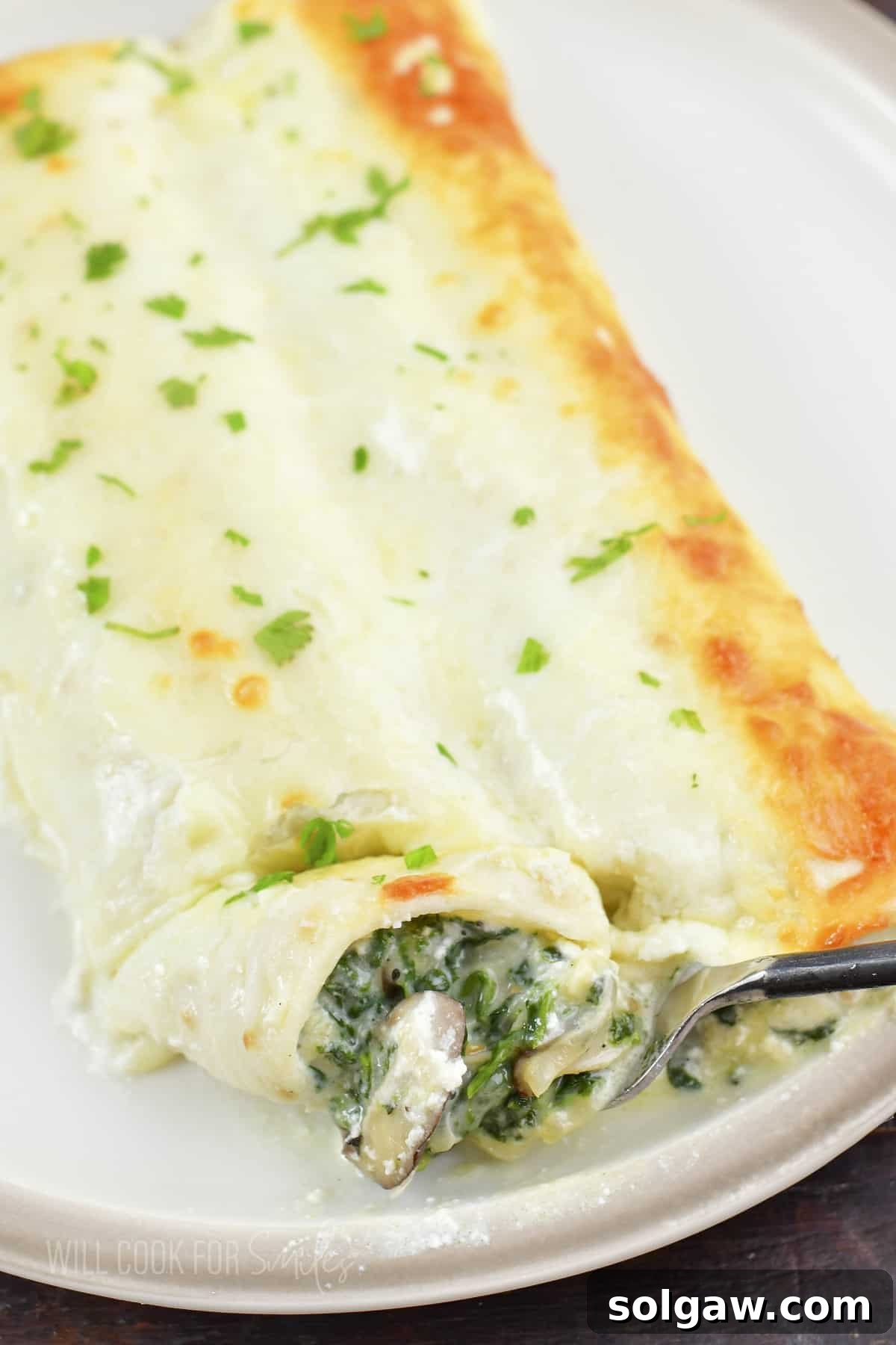 cutting some of the enchilada off with a fork, revealing the creamy spinach and mushroom filling.