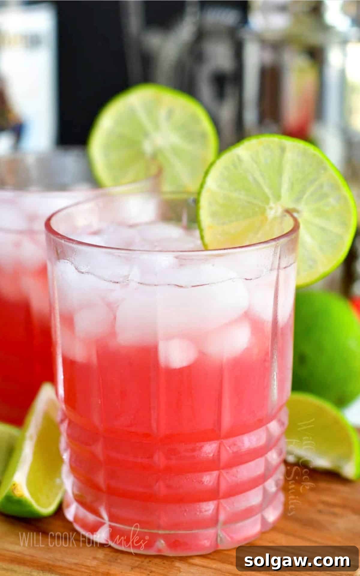 Pink Bay Breeze cocktail in a rocks glass with ice and a lime wheel on the rim, set against a blurred tropical background.