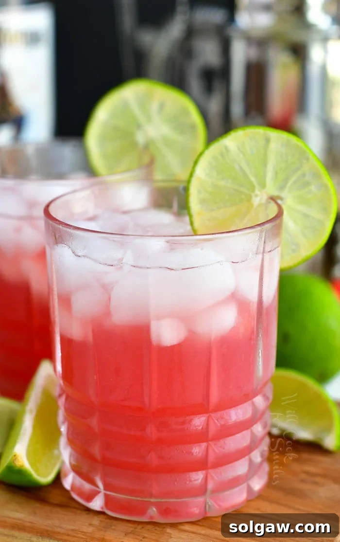 Front view of a glass filled with a bright pink Bay Breeze cocktail, ice, and a refreshing lime slice on the rim.