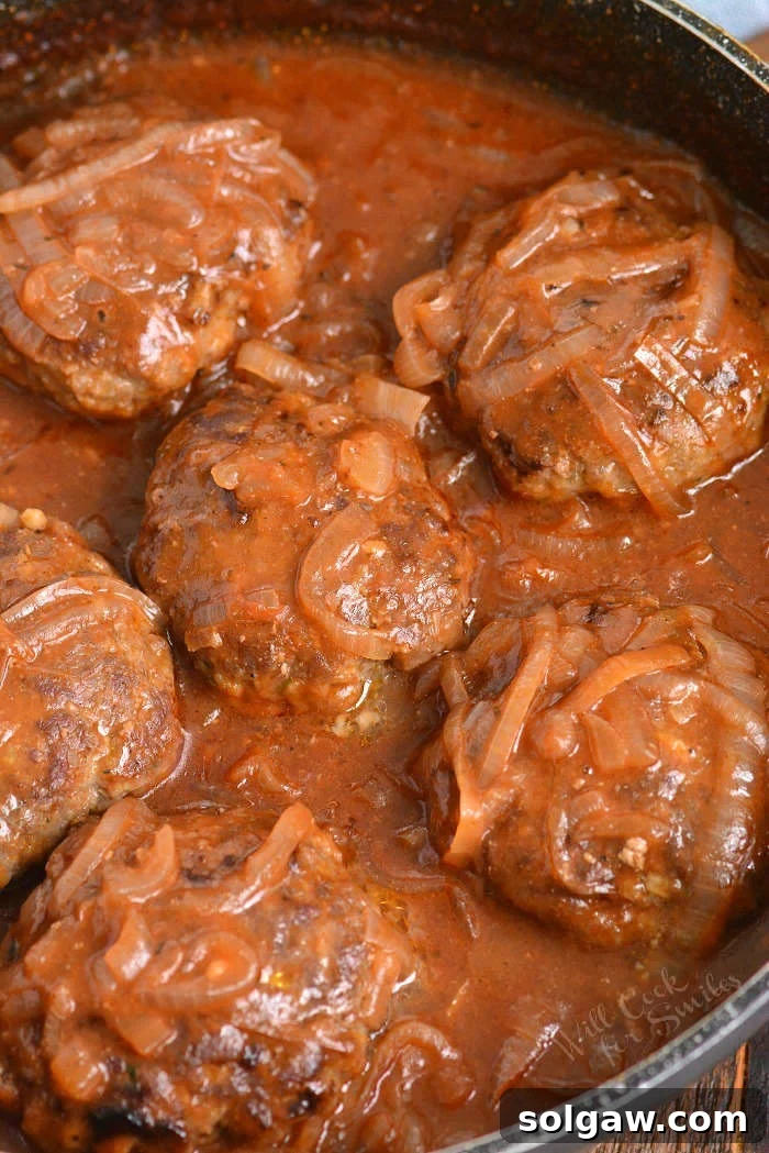 Six Salisbury steak patties in the pan cooking in French onion sauce. A comforting and rich dish.