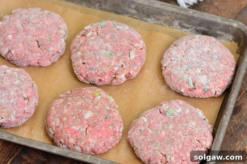 Prepped and shaped raw Salisbury steak patties on parchment paper in a baking sheet, ready for searing.