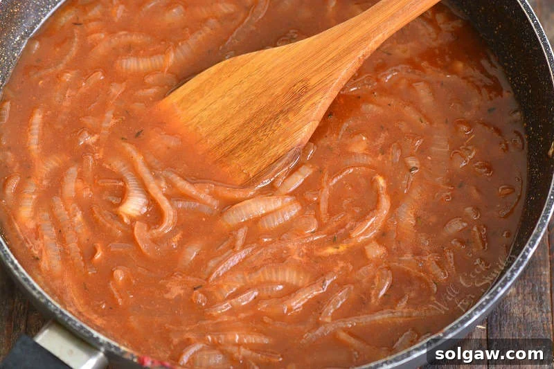Cooking the French Onion sauce in the cooking pan, stirring with a wooden spatula to scrape up flavorful bits.