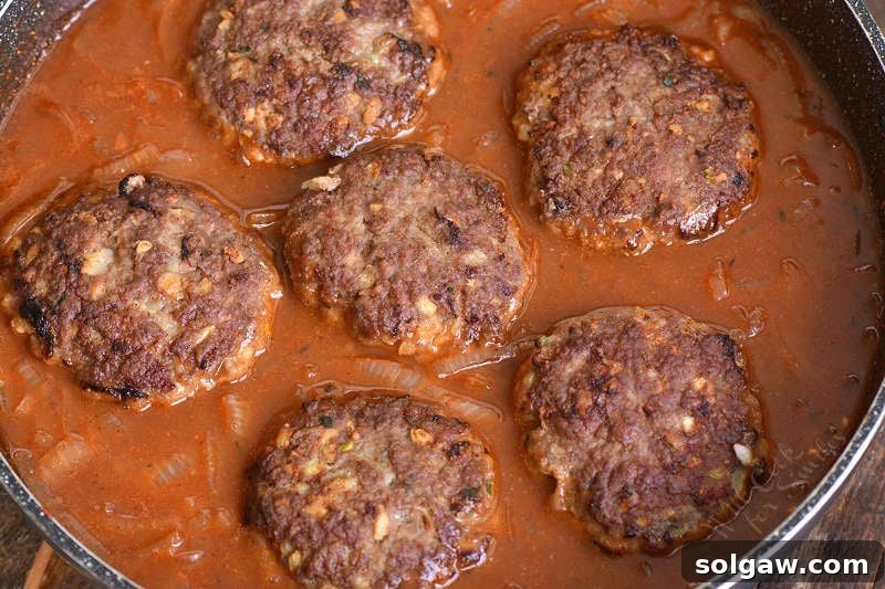 Adding partially cooked Salisbury steaks into the pan with the rich French onion sauce, ready to simmer.
