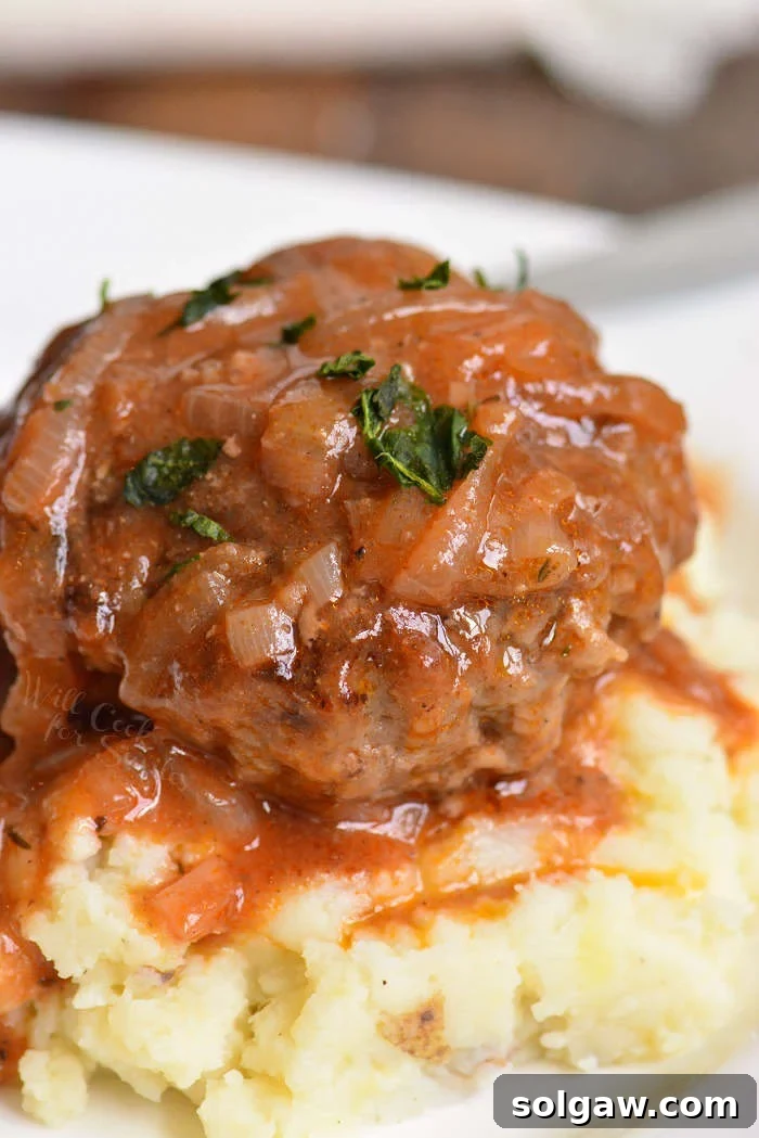 Large and juicy French onion Salisbury steak on top of fluffy mashed potatoes, garnished with fresh herbs.