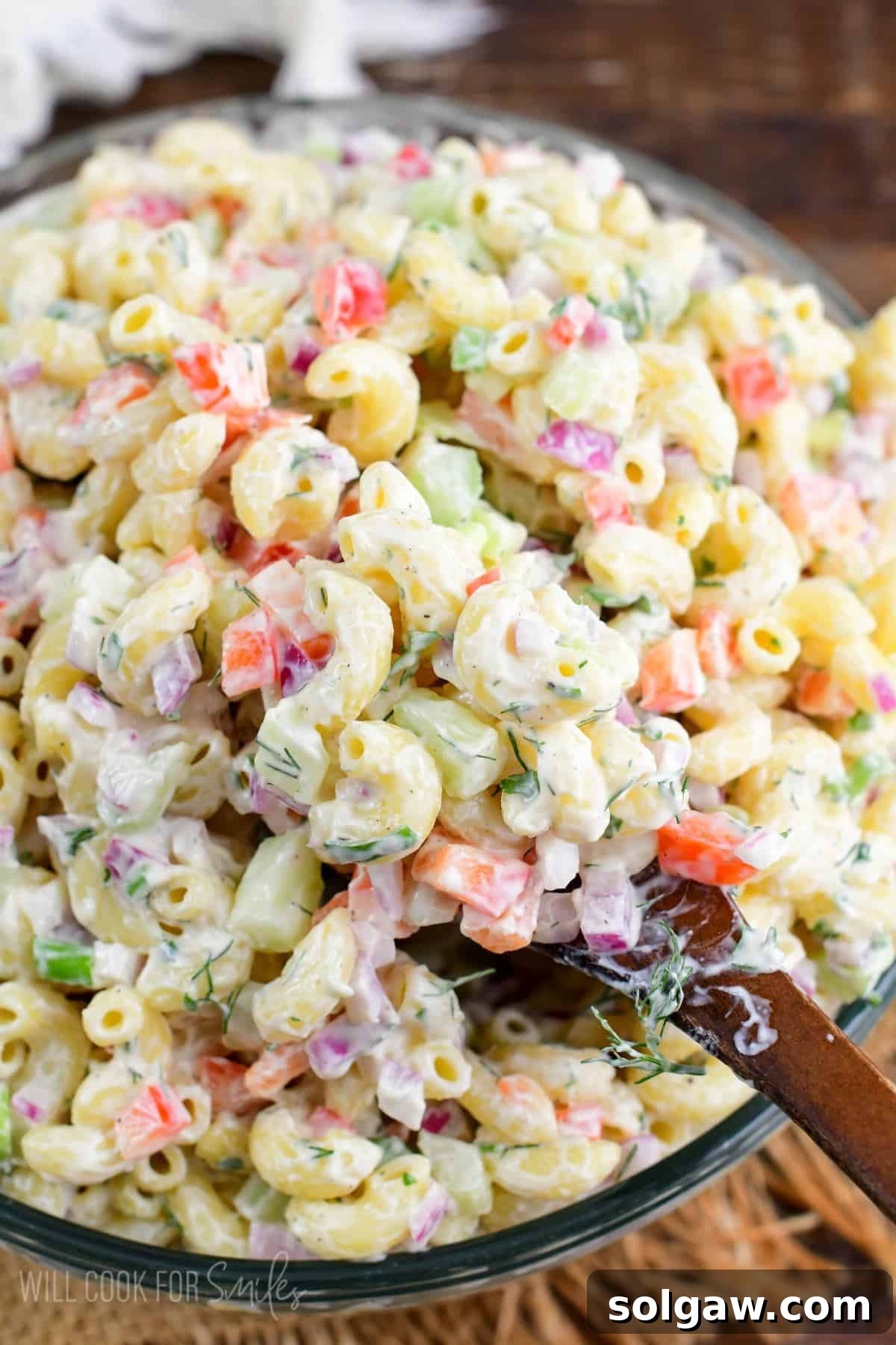 Homestyle Macaroni Salad 6 A large serving bowl filled with creamy macaroni salad, with a wooden spoon scooping out a generous portion, ready to be enjoyed.