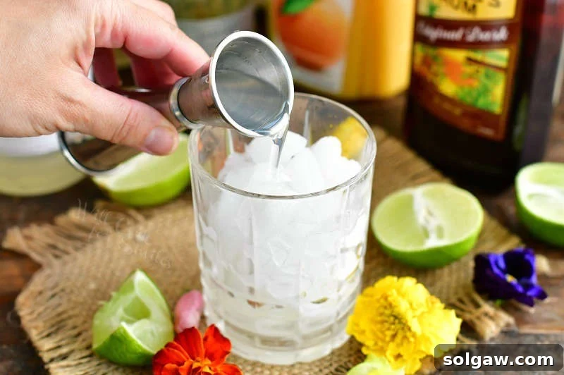 pouring in orgeat syrup into the glass with crushed ice out of a silver measuring cup