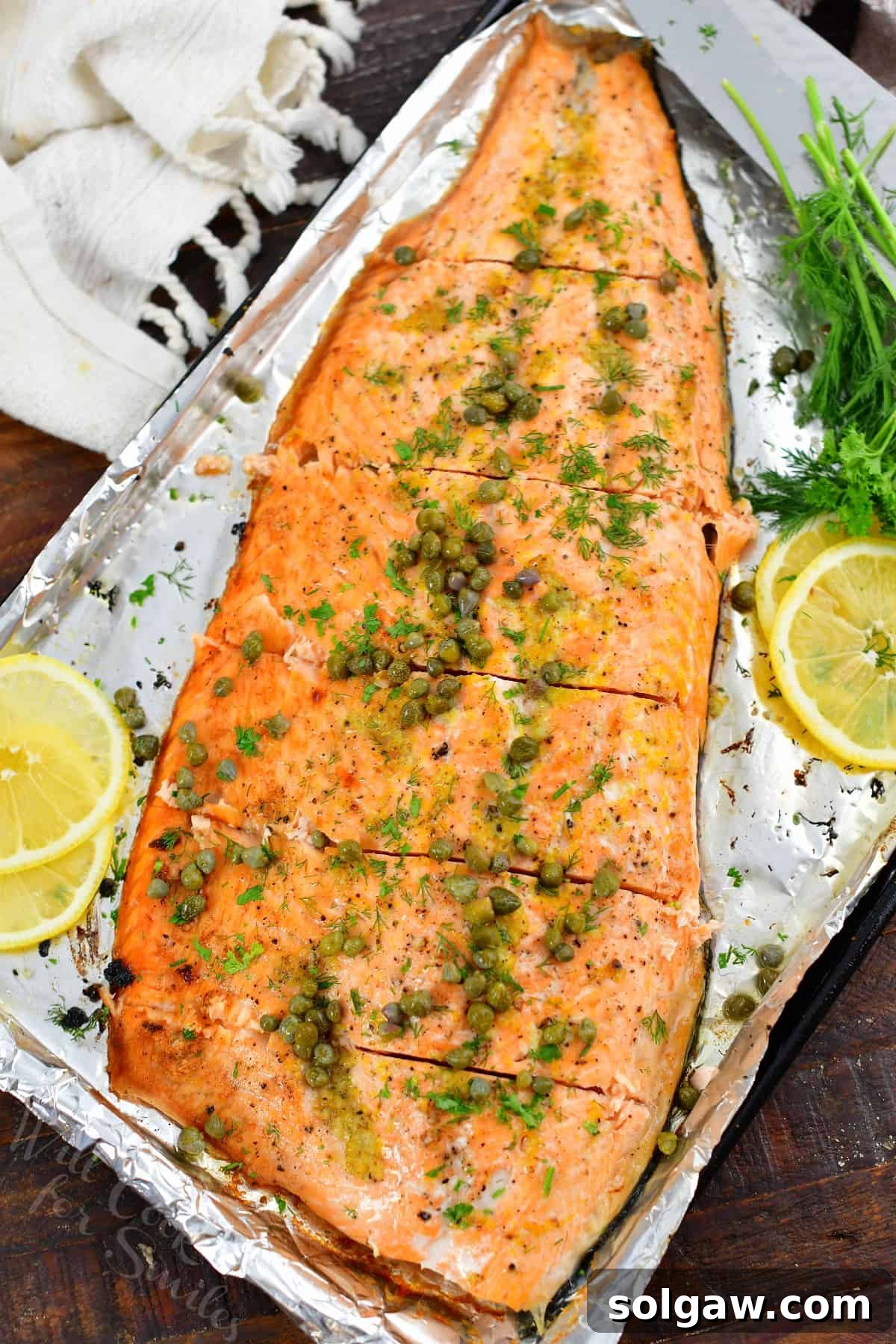 Top view of a whole baked salmon topped with capers and sliced lemons, ready for serving.