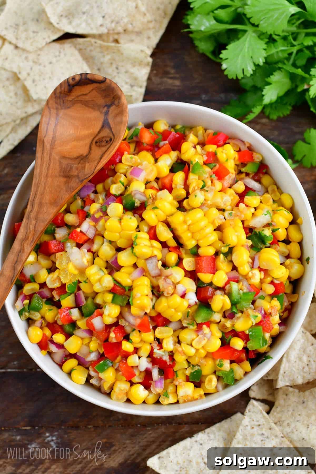 Vibrant corn salsa mixed in a white bowl, ready to be served, with a wooden spoon resting nearby.