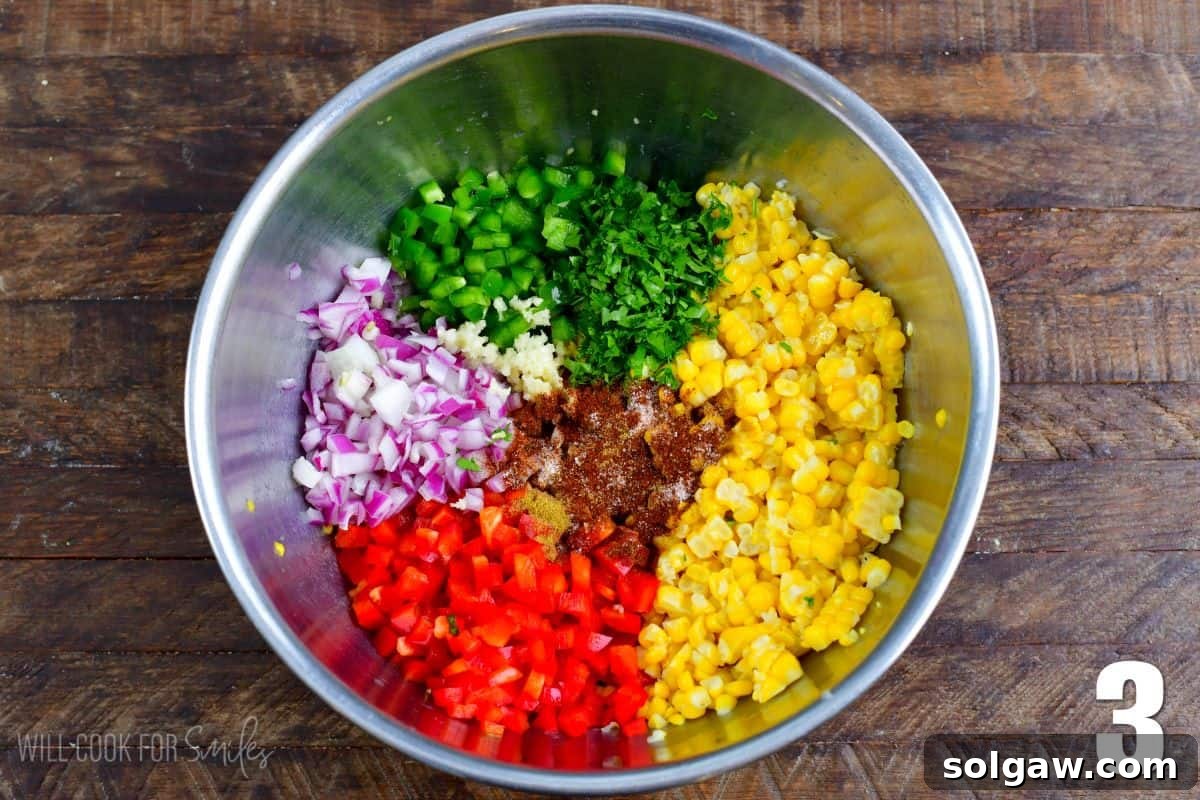 All the fresh ingredients for corn salsa are combined in a sleek metal bowl on a wooden surface, ready for mixing.