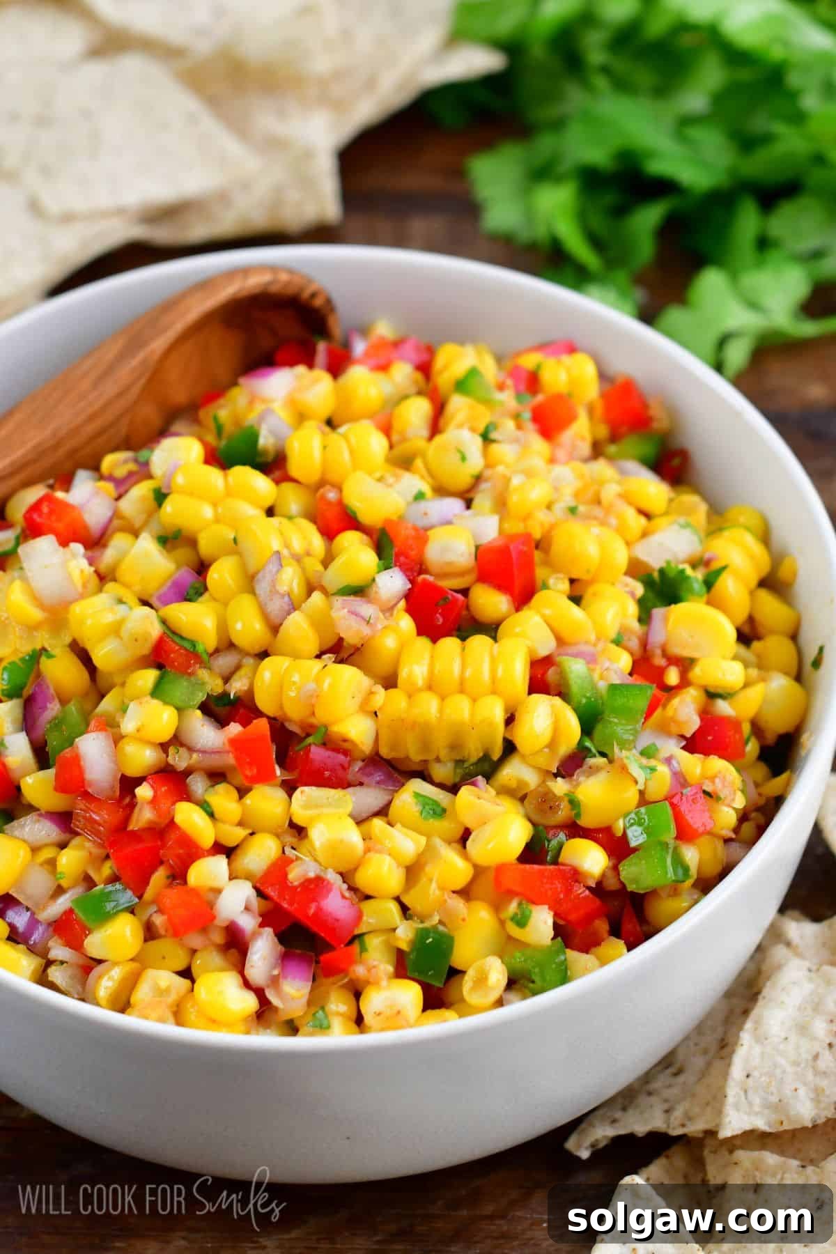 A white bowl brimming with fresh corn salsa, adorned with a wooden spoon, photographed from a flattering angle.