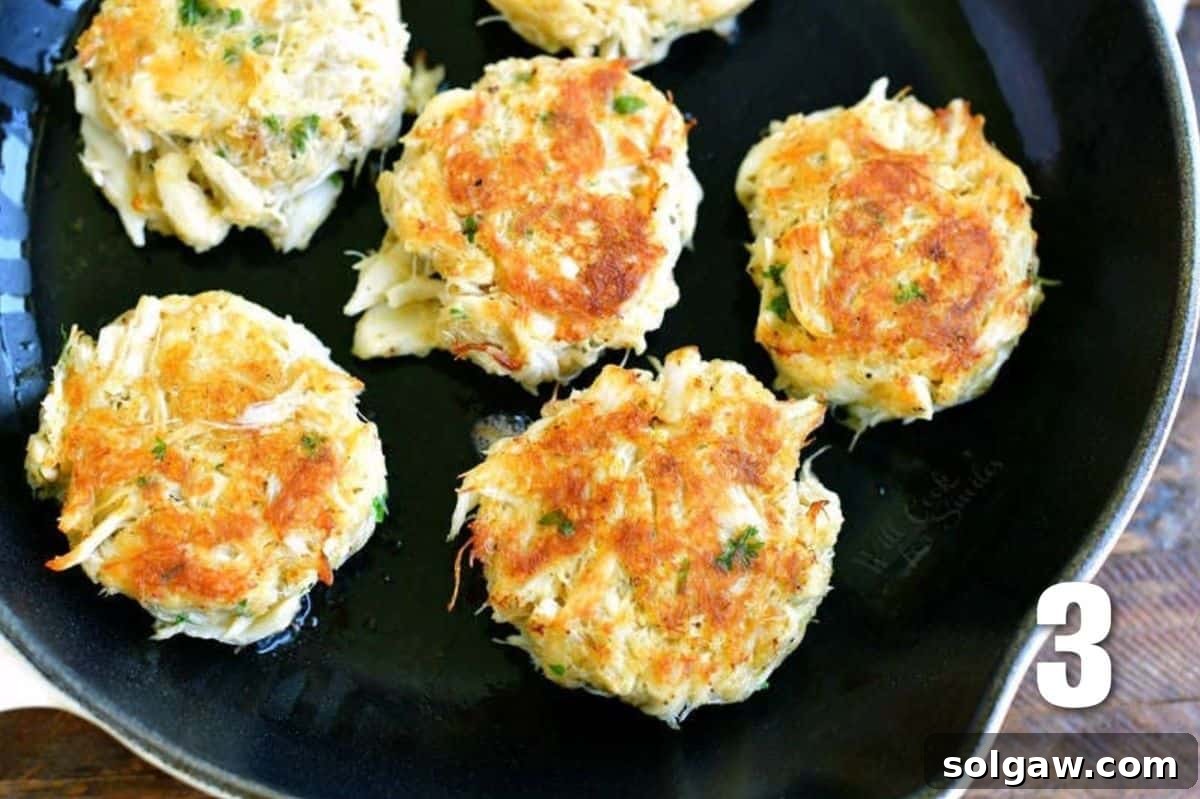 Close-up shot of several golden-brown crab cakes sizzling in a black skillet, indicating a delicious cooking process.