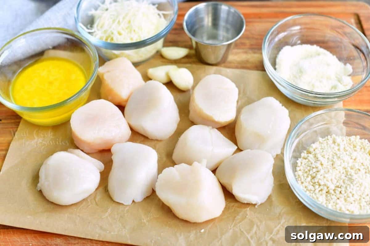 Fresh ingredients for baked scallops including scallops, butter, garlic, breadcrumbs, and Parmesan cheese, laid out on a baking dish.