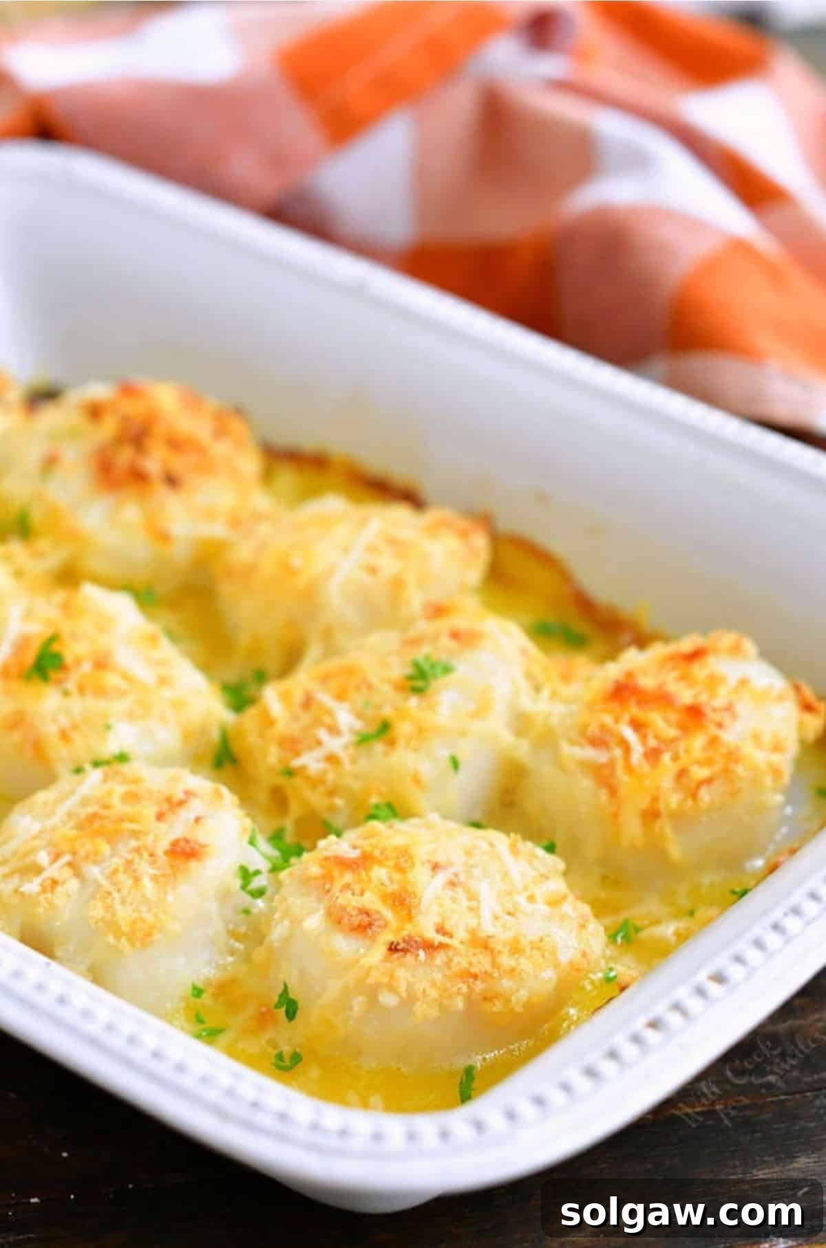 Several perfectly baked sea scallops in a white baking dish, coated in butter and Parmesan cheese, ready to serve.