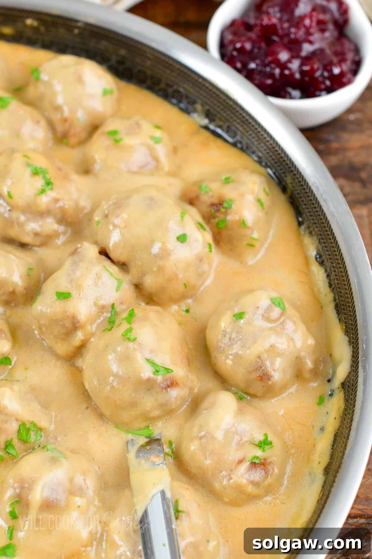 Several tender Swedish meatballs covered in creamy gravy in a pan with a metal spoon, inviting you to serve.