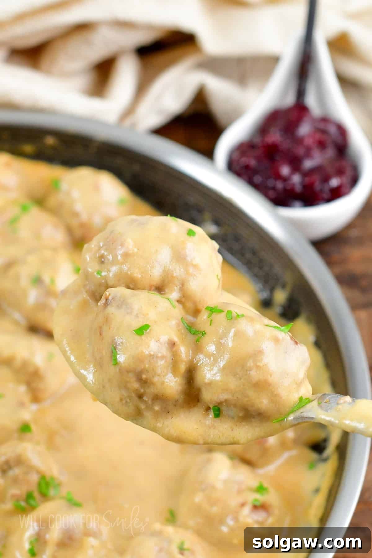 Creamy Swedish Meatballs 8 A metal spoon lifts a succulent Swedish meatball, perfectly coated in creamy brown gravy, from a serving dish, highlighting its appetizing texture.