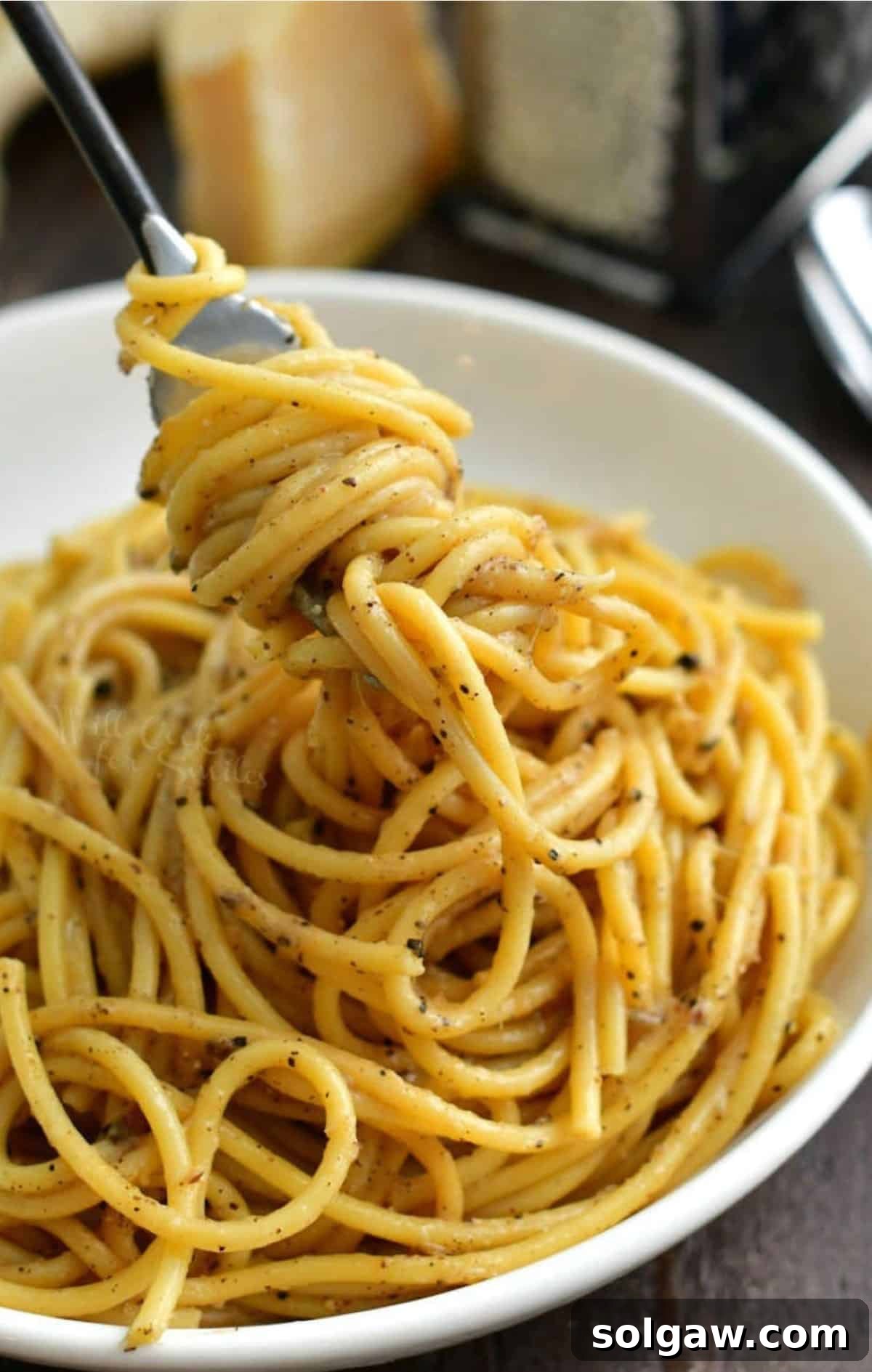 The Creamy Pepper Parmesan Pasta 2 Swirling a generous portion of cheesy cacio e pepe pasta onto a fork from a rustic bowl, showcasing its creamy texture and rich pepper flecks.