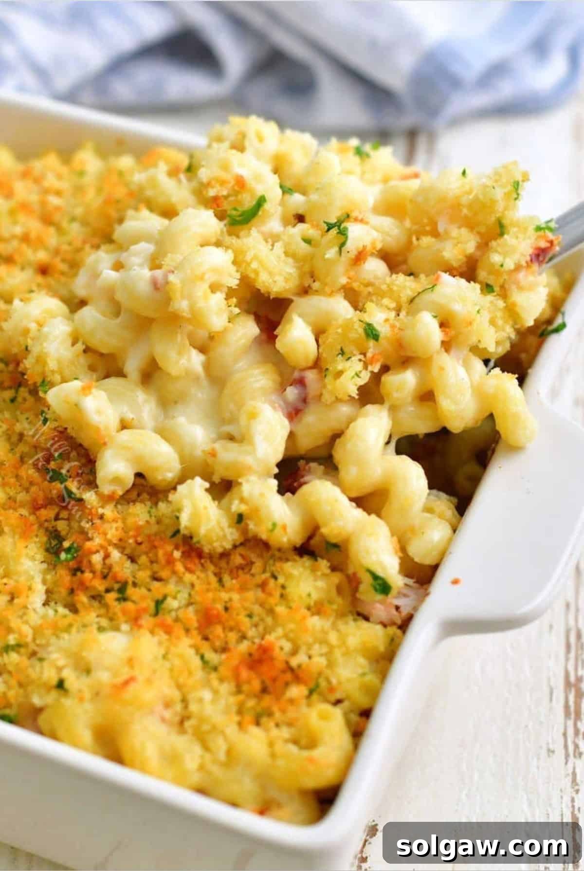 Gourmet Lobster Mac 2 Scooping out some golden, bubbling lobster mac and cheese from a baking pan with a ladle.