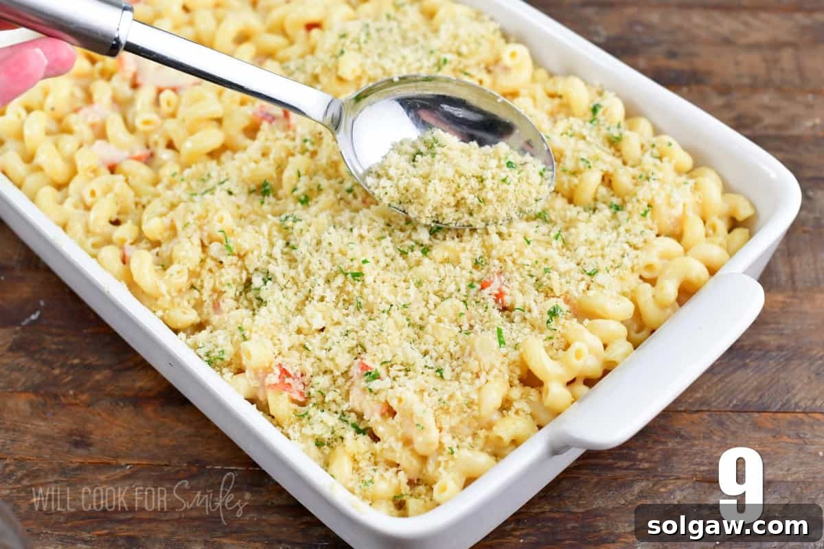 Gourmet Lobster Mac 7 Sprinkling buttery Panko topping over the mac and cheese in a baking dish with a silver spoon.