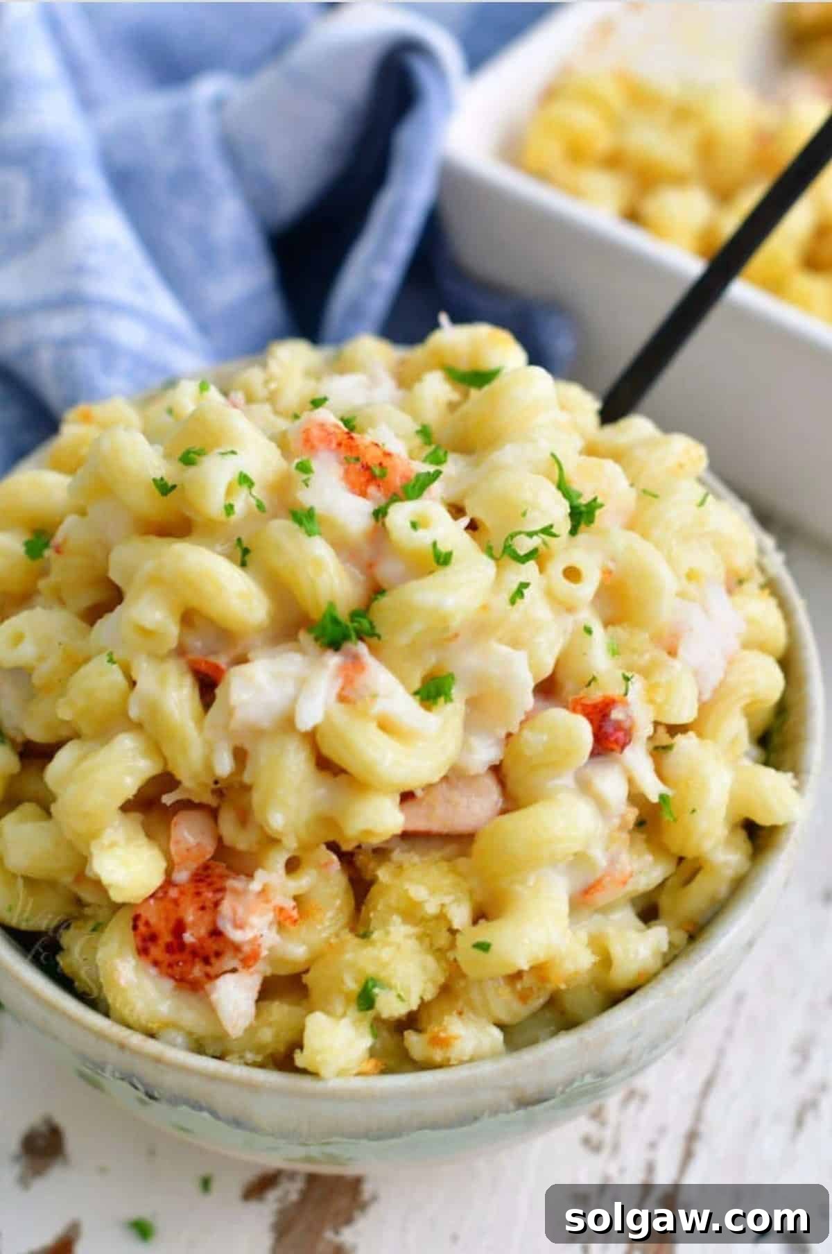 Gourmet Lobster Mac 10 A bowl full of lobster mac and cheese next to the baking dish and a fork, highlighting the rich texture.