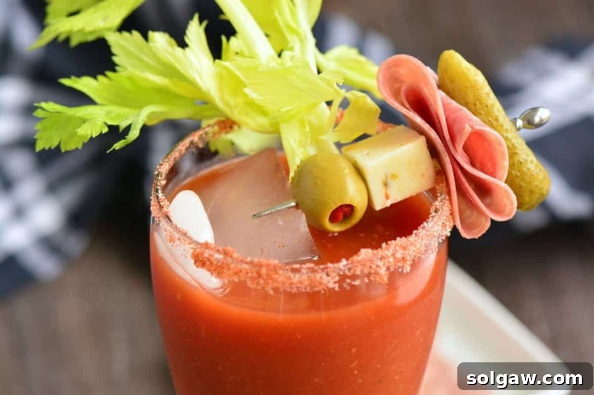 Close-up of a Bloody Mary glass generously garnished with cheese, an olive, salami, and a pickle on a skewer.