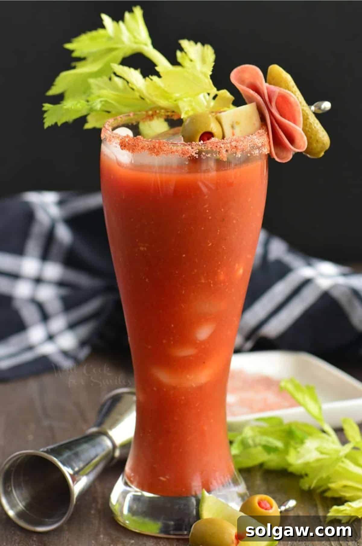 Tall glass of Bloody Mary with celery and a garnish of cheese, olive, salami, and pickle